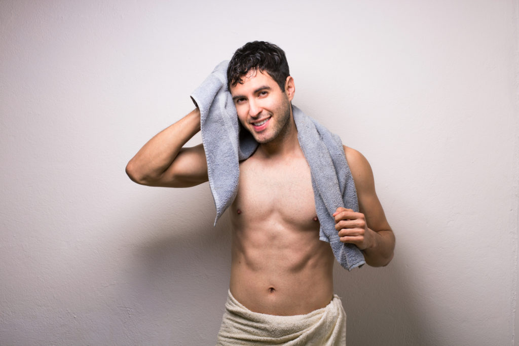 Ung mann som tørker seg på håret og i nakken etter dusjing.