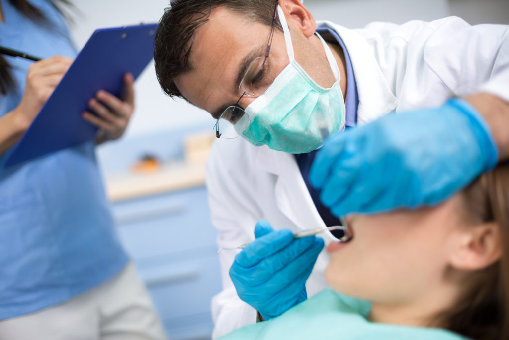 Mannlig tannlege sjekker tennene til en pasient.