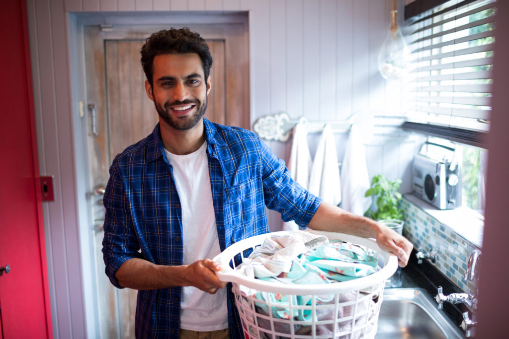 Ung mann som bærer en vaskekurv med klesvask.