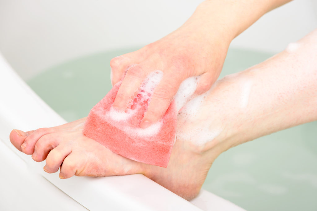 Hånd som holder en svamp med såpe, og som vasker føttene i badekar.