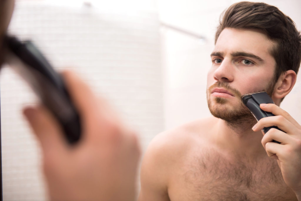 Ung mann med skjegg-trimmer foran speilet.