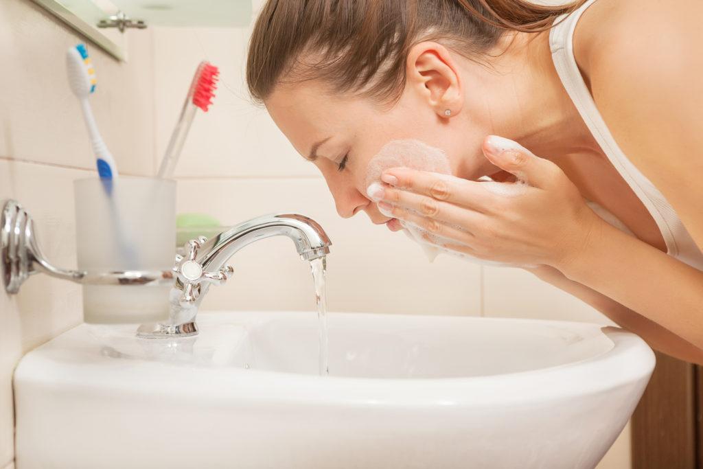 Ung kvinne vasker ansiktet med vann.